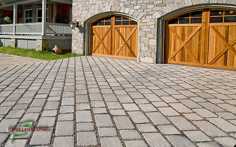 A driveway with wooden garage doors and brick pavers.
