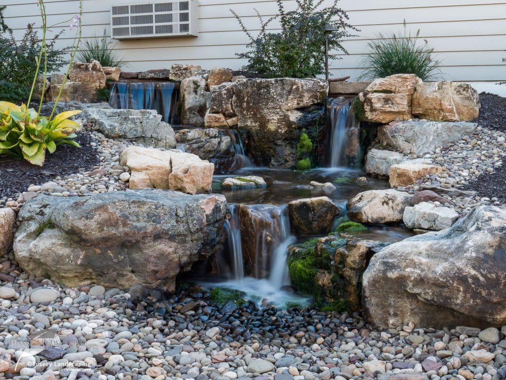 A small waterfall in a backyard with rocks and gravel.