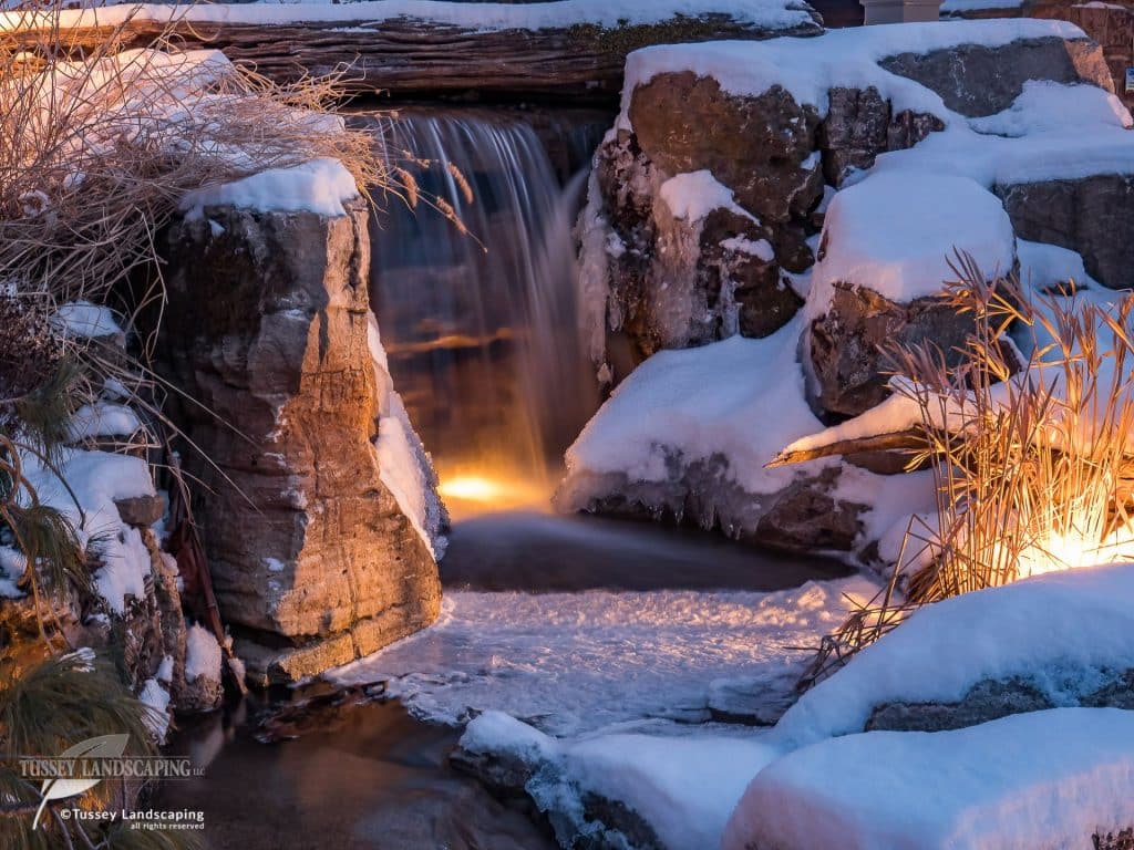 A small waterfall in a snow covered garden.