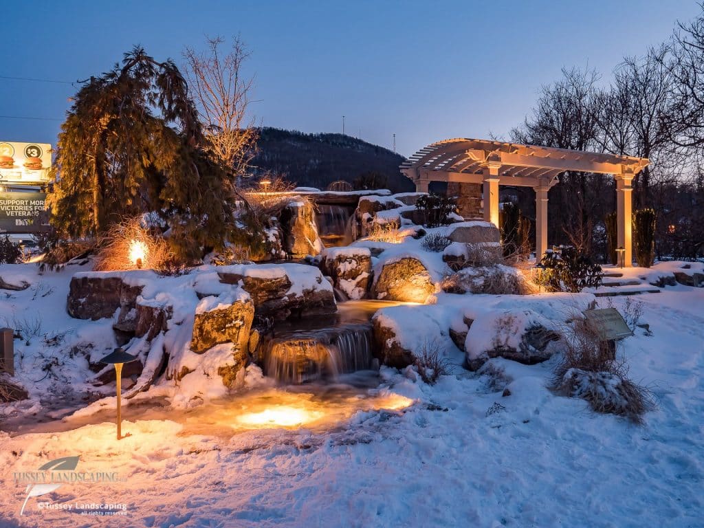 A snow covered landscape with a waterfall and gazebo.