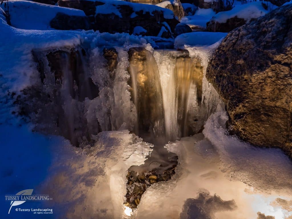 A waterfall is lit up at night in a snow covered area.