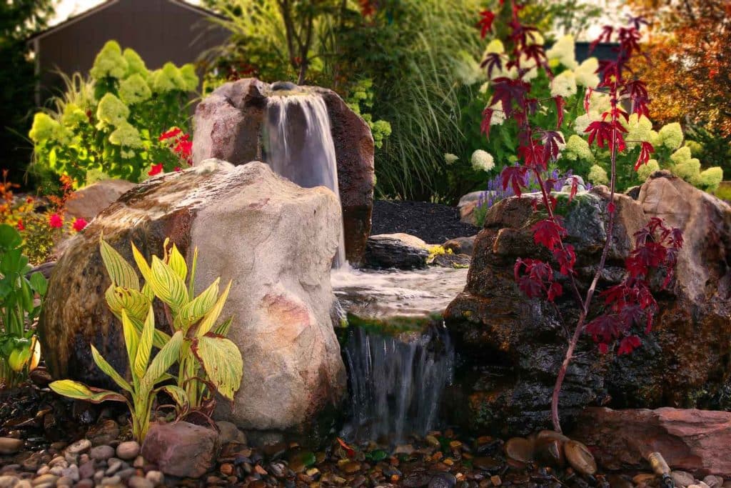 A waterfall in a garden with rocks and plants.