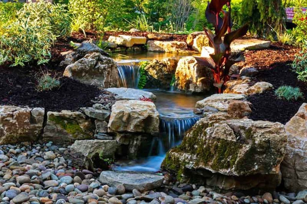 A waterfall in a garden with rocks and plants.