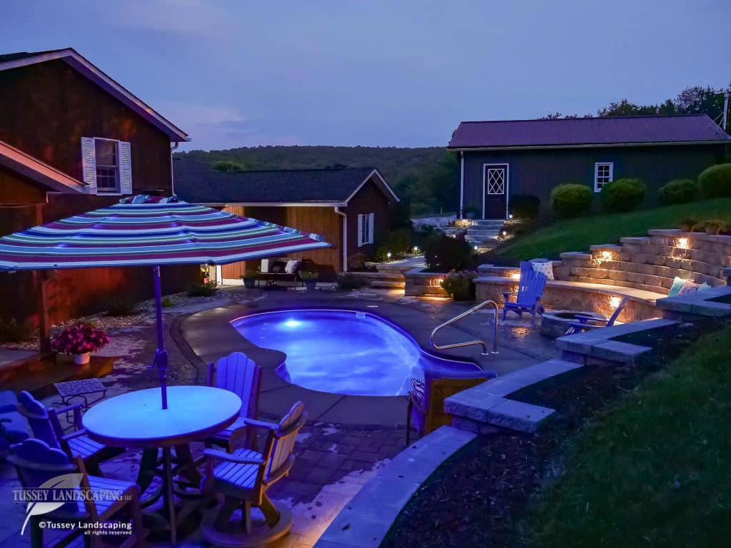 A backyard with a pool and patio furniture at night.