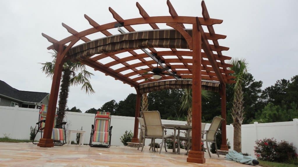 A wooden pergola in a backyard with a table and chairs.