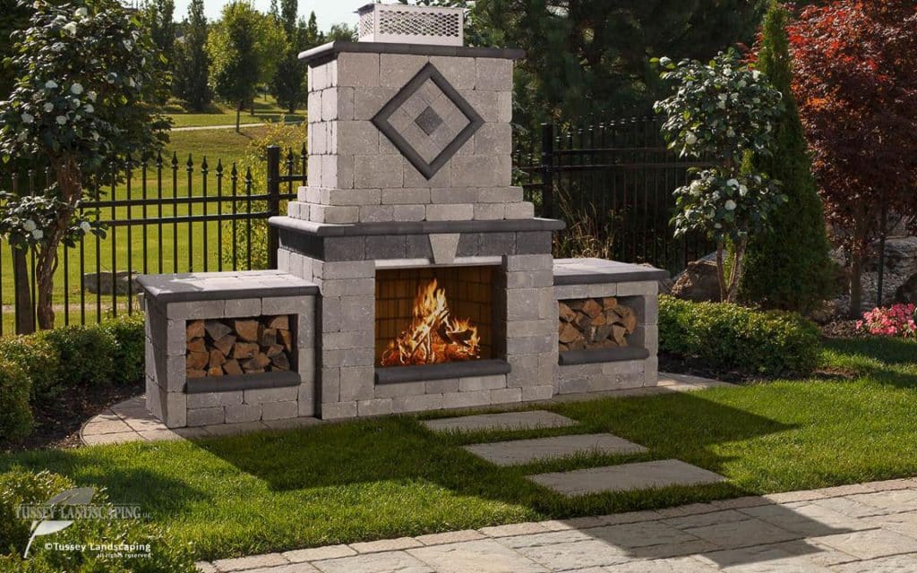 A stone fireplace in a backyard with a fire pit.