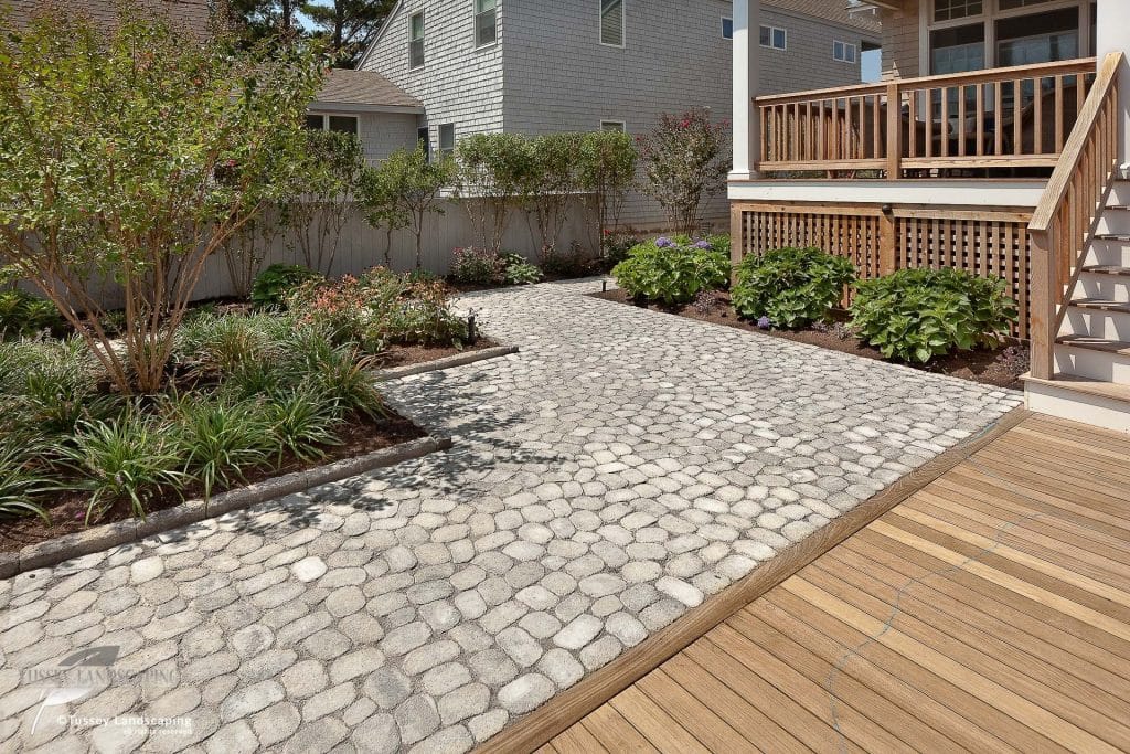 A backyard with a wooden deck and stone walkway.