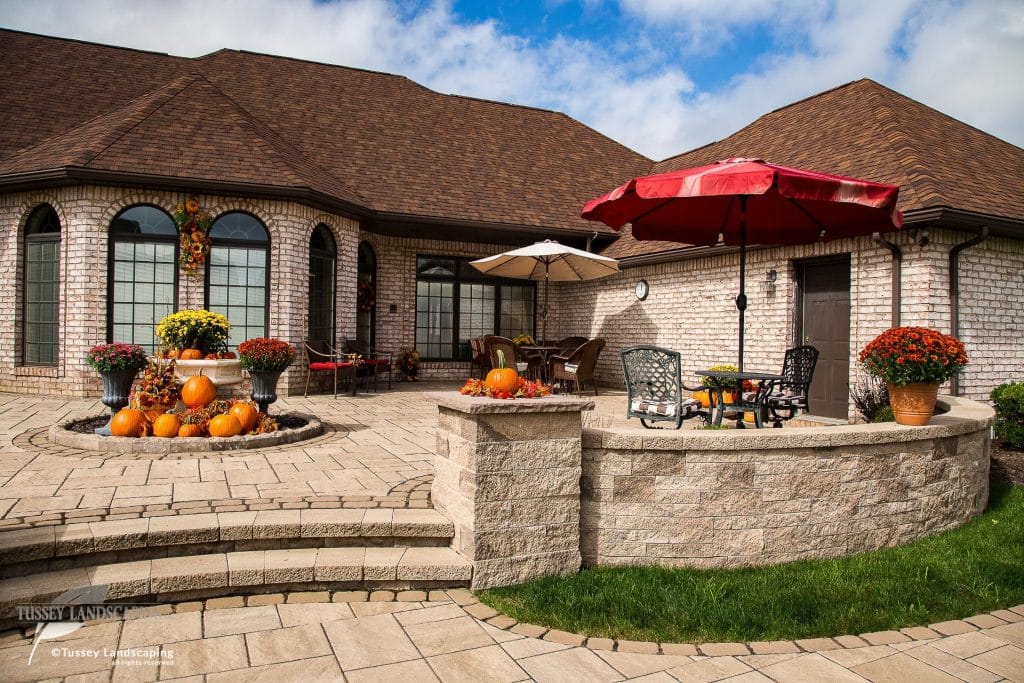 A patio with pumpkins and an umbrella.