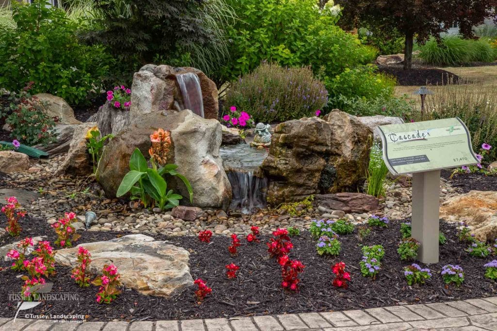 A rock garden with flowers and a sign.