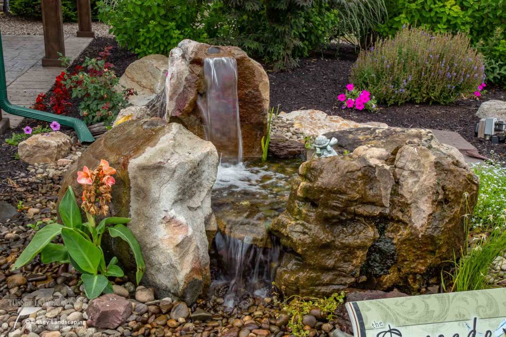 A rock waterfall in a garden with a sign.