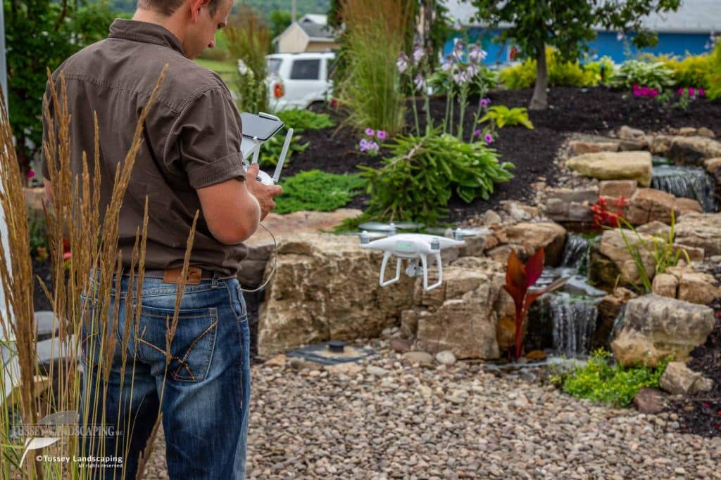 A man holding a drone in front of a waterfall.