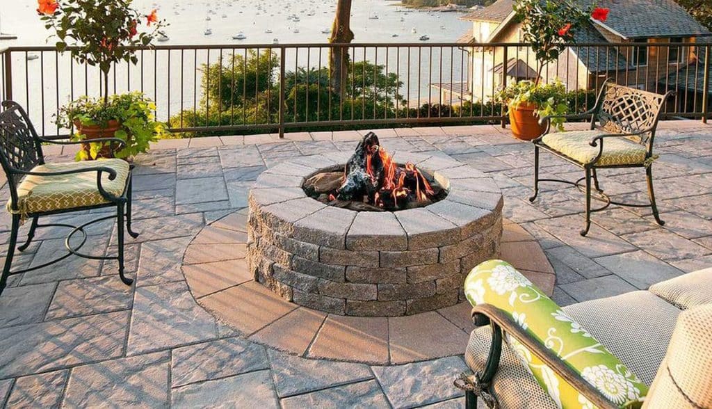 A patio with a fire pit and furniture overlooking the water.