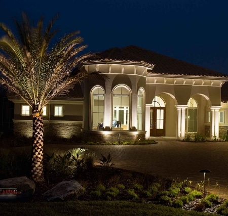 A home is lit up at night with palm trees.