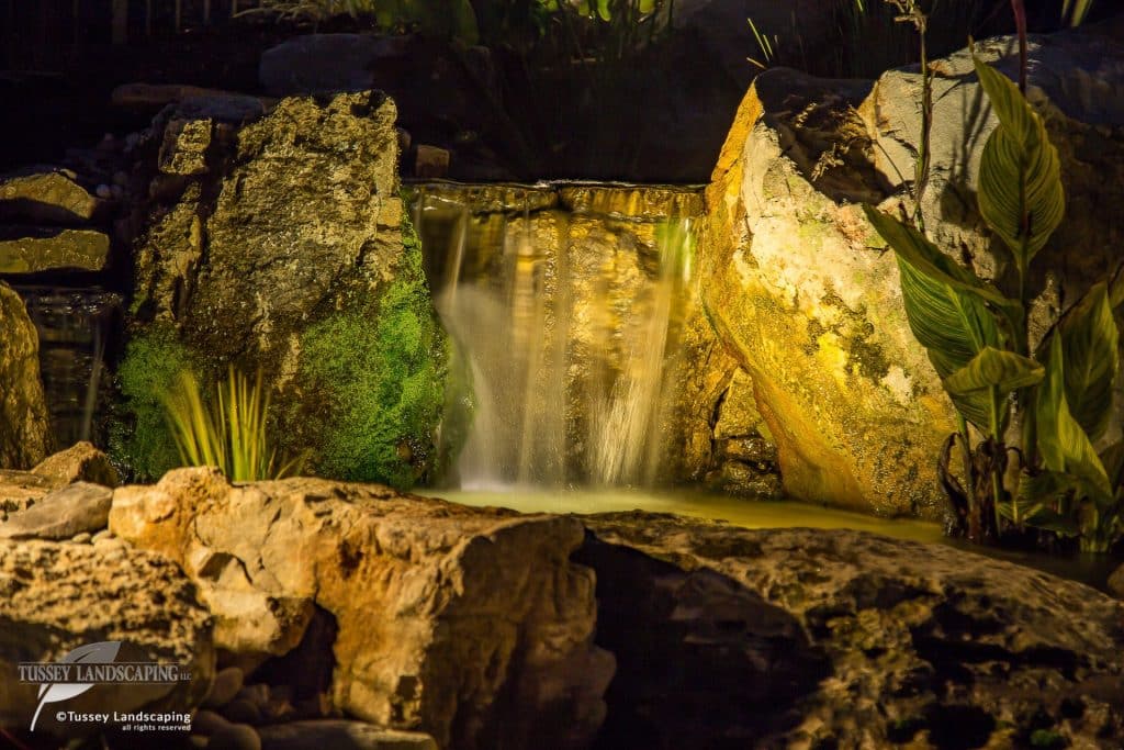 A waterfall in the middle of a rock garden at night.