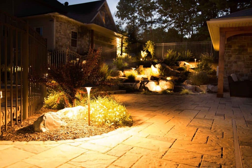A stone walkway with lighting at dusk in a backyard.