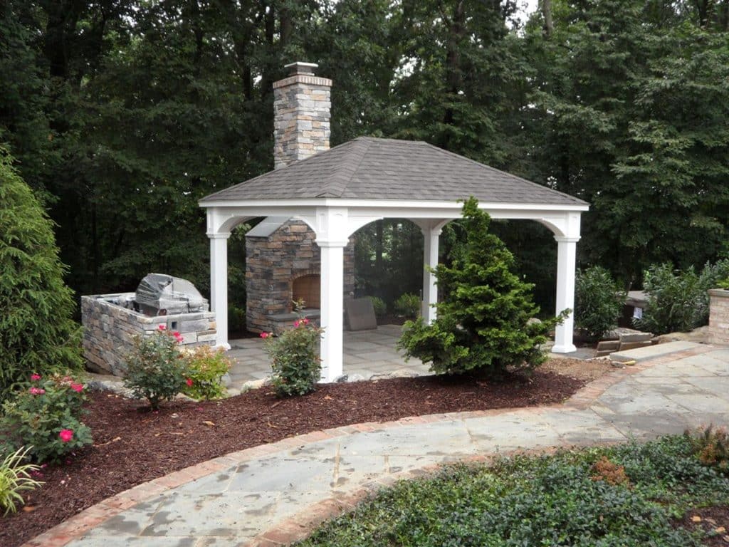 A gazebo with a fireplace in the middle of a yard.