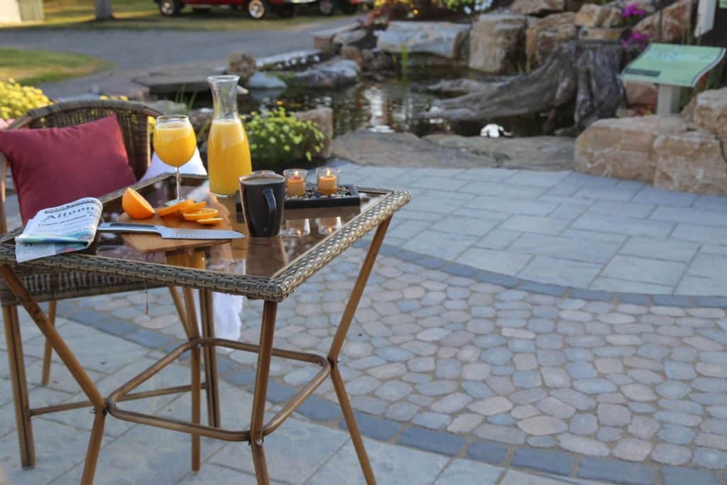 A table with a cup of orange juice and a wicker chair.