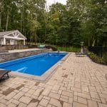 Fiberglass swimming pool with spillway paver patio and pool house and outdoor living space