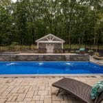 Fiberglass swimming pool with spillway paver patio and pool house and outdoor living space