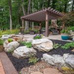 pergola on paver patio with natural stone stairs, landscaping, and mountain boulders