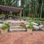 pergola on paver patio with natural stone stairs, landscaping, and mountain boulders