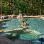 swim pond with retaining wall, paver patio, landscaping, water feature, and waterfalls
