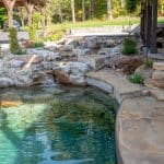 swim pond with retaining wall, paver patio, landscaping, water feature, and waterfalls