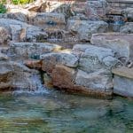 swim pond with retaining wall, paver patio, landscaping, water feature, and waterfalls