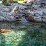 swim pond with retaining wall, paver patio, landscaping, water feature, and waterfalls