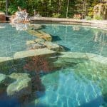 swim pond with retaining wall, paver patio, landscaping, water feature, and waterfalls
