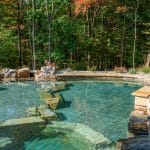 swim pond with retaining wall, paver patio, landscaping, water feature, and waterfalls
