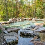 swim pond with retaining wall, paver patio, landscaping, water feature, and waterfalls