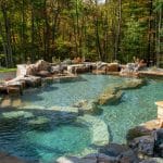 swim pond with retaining wall, paver patio, landscaping, water feature, and waterfalls