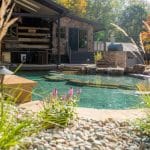 swim pond with retaining wall, paver patio, landscaping, water feature, and waterfalls