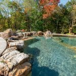 swim pond with retaining wall, paver patio, landscaping, water feature, and waterfalls