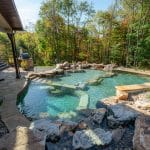 swim pond with retaining wall, paver patio, landscaping, water feature, and waterfalls