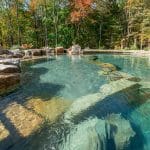 swim pond with retaining wall, paver patio, landscaping, water feature, and waterfalls