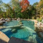 swim pond with retaining wall, paver patio, landscaping, water feature, and waterfalls