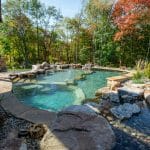 swim pond with retaining wall, paver patio, landscaping, water feature, and waterfalls