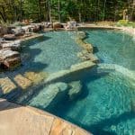 swim pond with retaining wall, paver patio, landscaping, water feature, and waterfalls