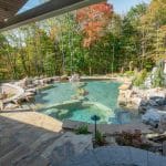 swim pond with retaining wall, paver patio, landscaping, water feature, and waterfalls