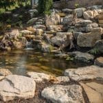 pond with mountain boulders and stream beside a flagstone patio
