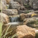 pond with mountain boulders and stream beside a flagstone patio
