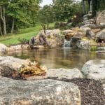 pond with mountain boulders and stream beside a flagstone patio