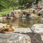 pond with mountain boulders and stream beside a flagstone patio