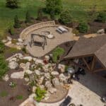 outdoor living space with in ground swimming pool, water falls, water feature, patio, pavers, pavilion, fire pit, natural stone stairs, and retaining walls