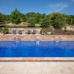 outdoor living space with in ground swimming pool, water falls, water feature, patio, pavers, pavilion, fire pit, natural stone stairs, and retaining walls