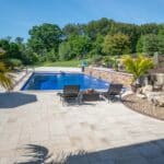 outdoor living space with in ground swimming pool, water falls, water feature, patio, pavers, pavilion, fire pit, natural stone stairs, and retaining walls