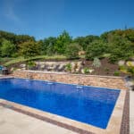 outdoor living space with in ground swimming pool, water falls, water feature, patio, pavers, pavilion, fire pit, natural stone stairs, and retaining walls