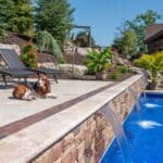 outdoor living space with in ground swimming pool, water falls, water feature, patio, pavers, pavilion, fire pit, natural stone stairs, and retaining walls